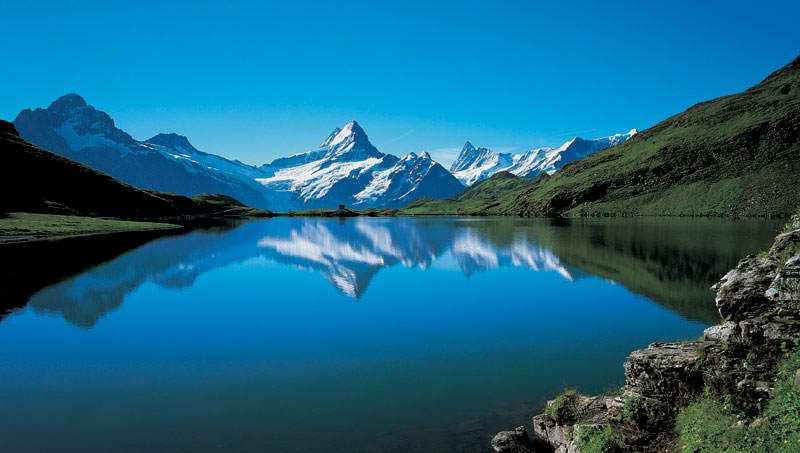 blue lake perfectly reflecting a pyramid shape mountain in the background, surrounded by mountains