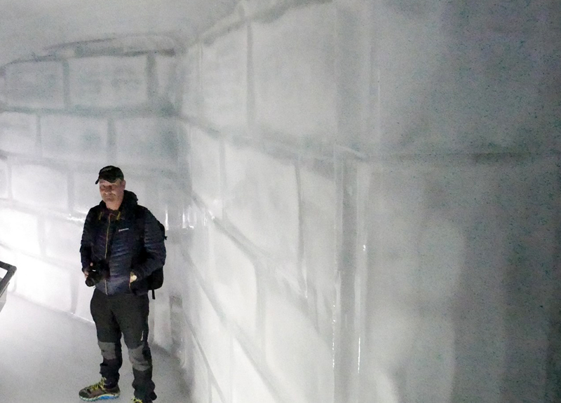 man standing in ice tunnel with wall made of large blocks of ice like bricks