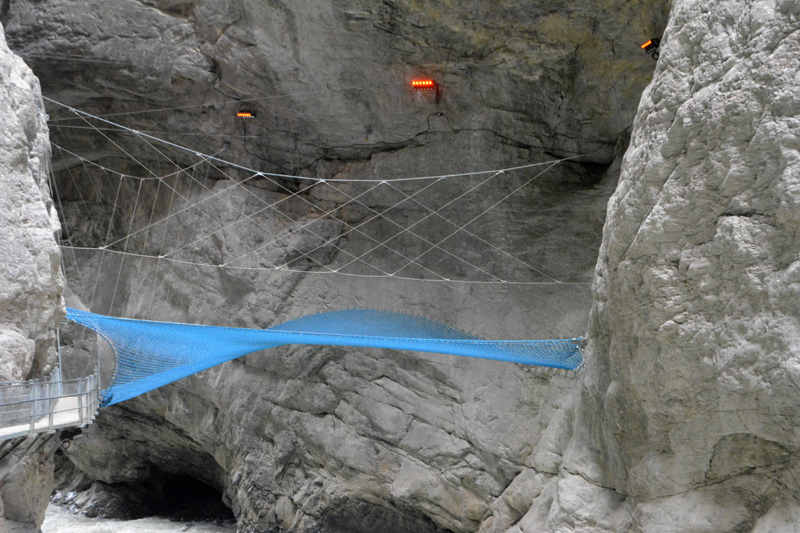 large blue net between 2 cliff walls in a canyon with a river below