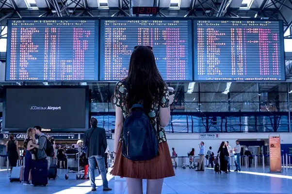 woman looking at departures and arrivals board at airport terminal